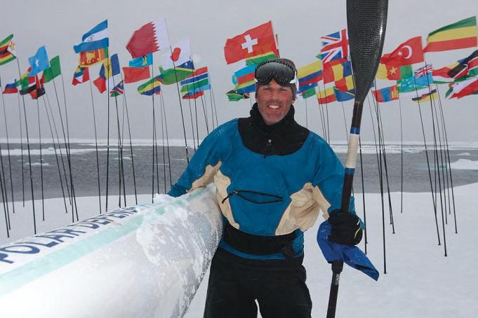Lewis standing on Arctic ice with his kayak in front of 192 flags