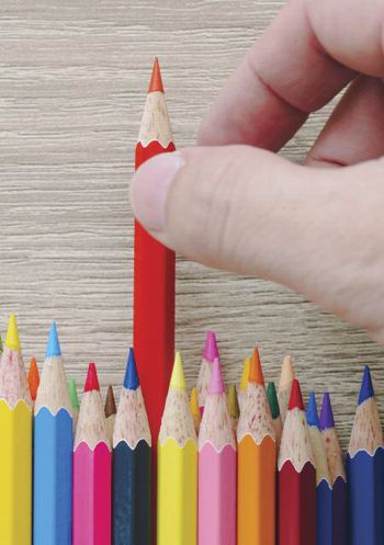 A hand picking up a coloured pencil from a line of different coloured pencils