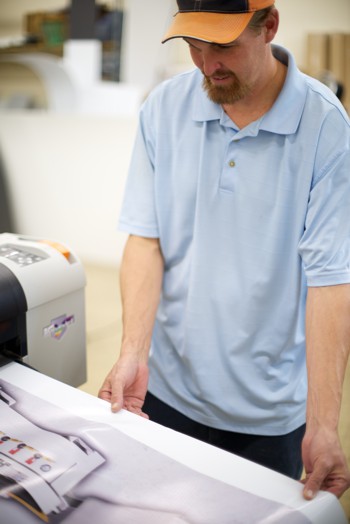 Man holding media as it comes out of a wide format printer.
