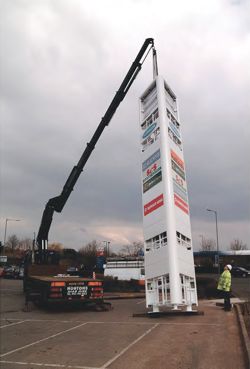 Gantry sign being installed by crane on the back of a lorry at a retail park.