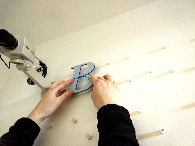 Flat cut letters being pushed onto locators on a wall.