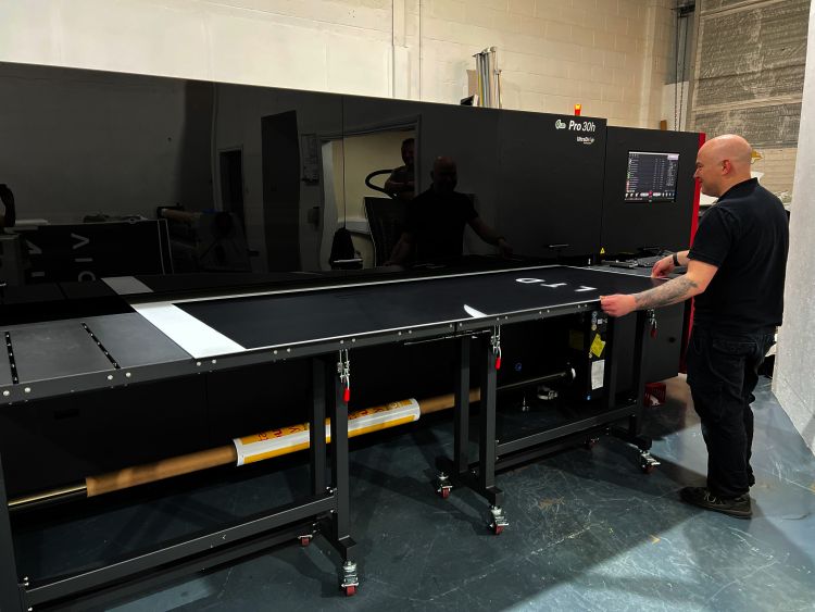A man stands in front of an EFI Vutek Pro 30h flatbed printer, readying material for print.