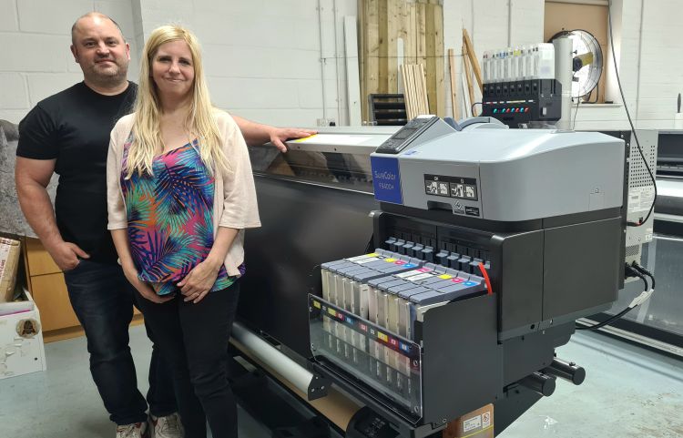 A man and woman stand side by side in a workshop next to an Epson Surecolour SC F9400H flatbed printer