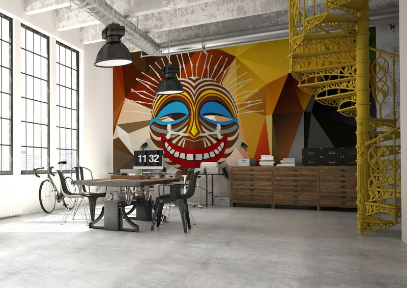 An open plan room with a spiral staircase and a brightly coloured mask print against the wall